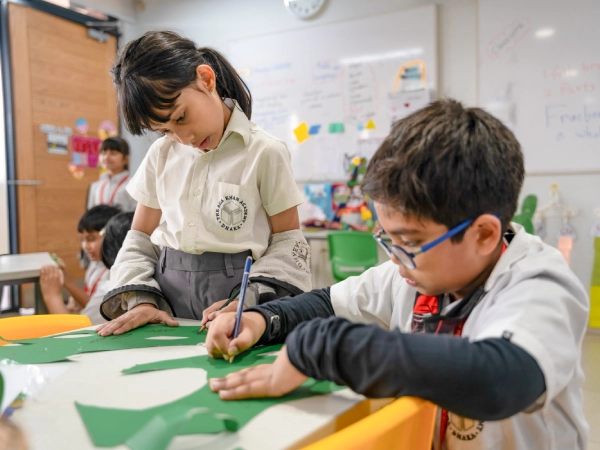 Front view of the Aga Khan Academy Dhaka’s red-brick academic building with students gathered below.   