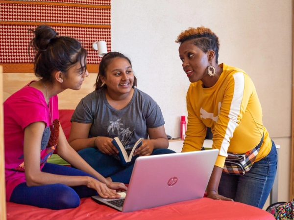 A teacher and a group of young students sit around a classroom table using colourful blocks and shapes to learn numbers and patterns during an interactive maths lesson.

