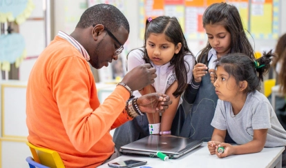 Students and a teacher work together on painting projects in an art classroom.