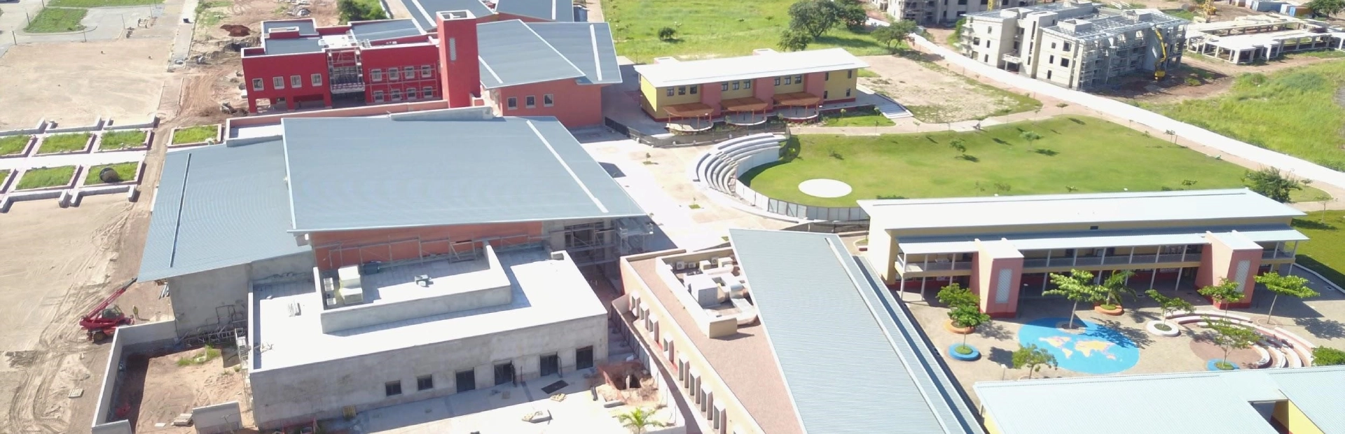 A group of students stand in formation on the school field performing morning exercises in front of the red-brick academic buildings under a clear sky.