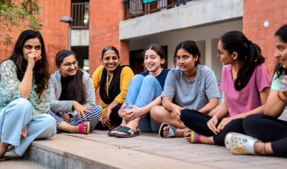 Residential students and dorm parents sitting outside together on the ground in front of the residences.