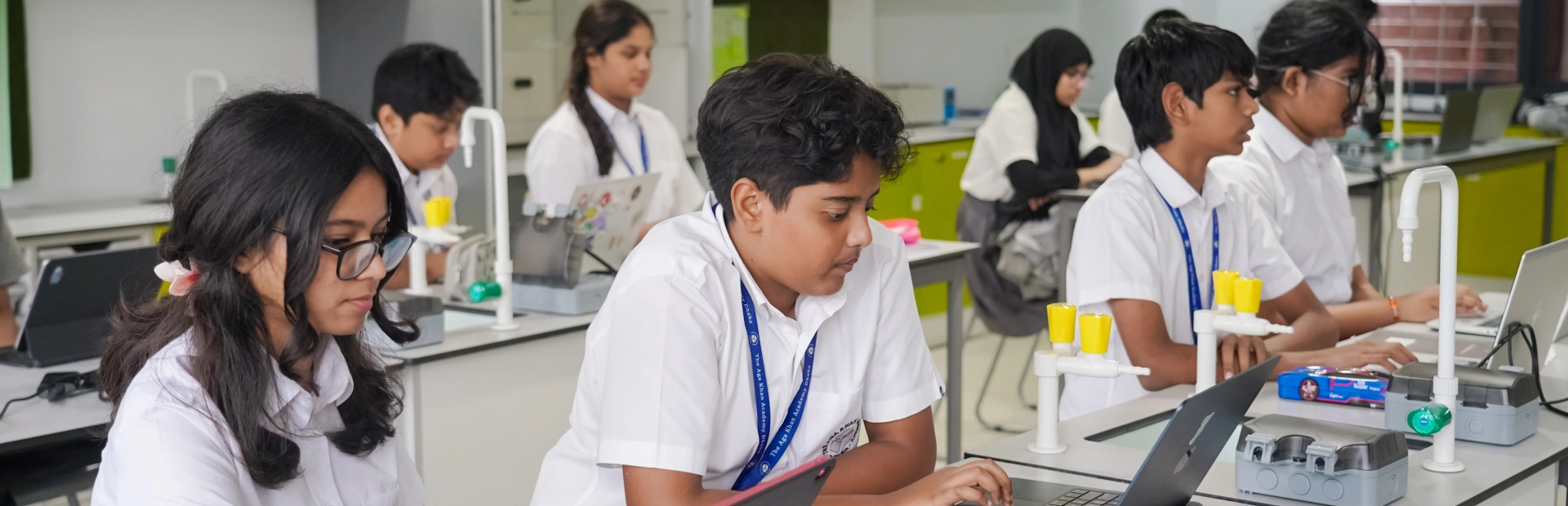 A group of MYP students sit at lab tables using laptops and tablets during a science lesson.