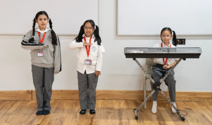 Three Junior School students perform during a classroom music activity, two standing and gesturing rhythmically while one plays an electronic keyboard.