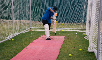 Student bats during cricket practice in a net enclosure.