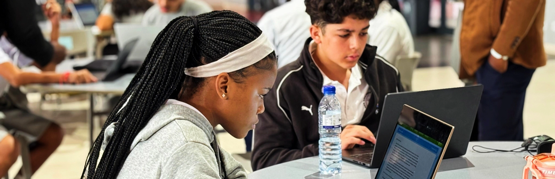 A group of MYP students sit at lab tables using laptops and tablets during a science lesson.
