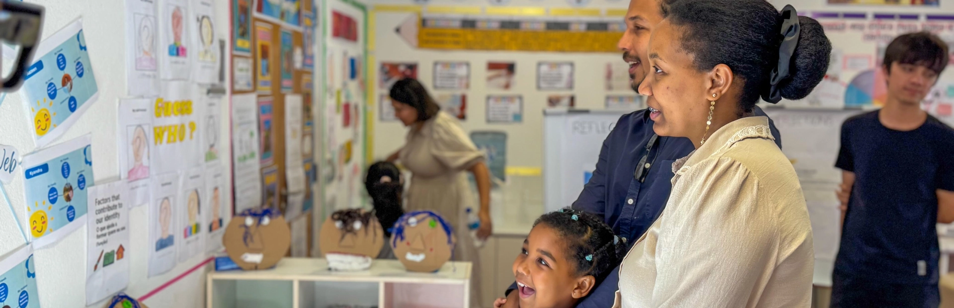 Parents and a child look at a student display on a classroom wall during an exhibition.