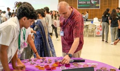 A student at the Aga Khan Academy Dhaka interacts with a teacher at a stall during Business Week, showcasing handmade products as part of an entrepreneurship activity.